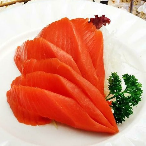 Freshly sliced Sockeye salmon served on a white plate, garnished with a sprig of parsley, ready for a gourmet meal