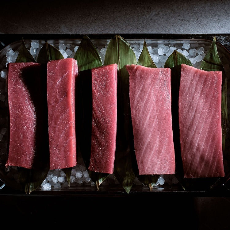 Assorted cuts of bluefin tuna displayed on a bed of ice with banana leaves underneath, emphasizing the fresh, premium quality of the fish