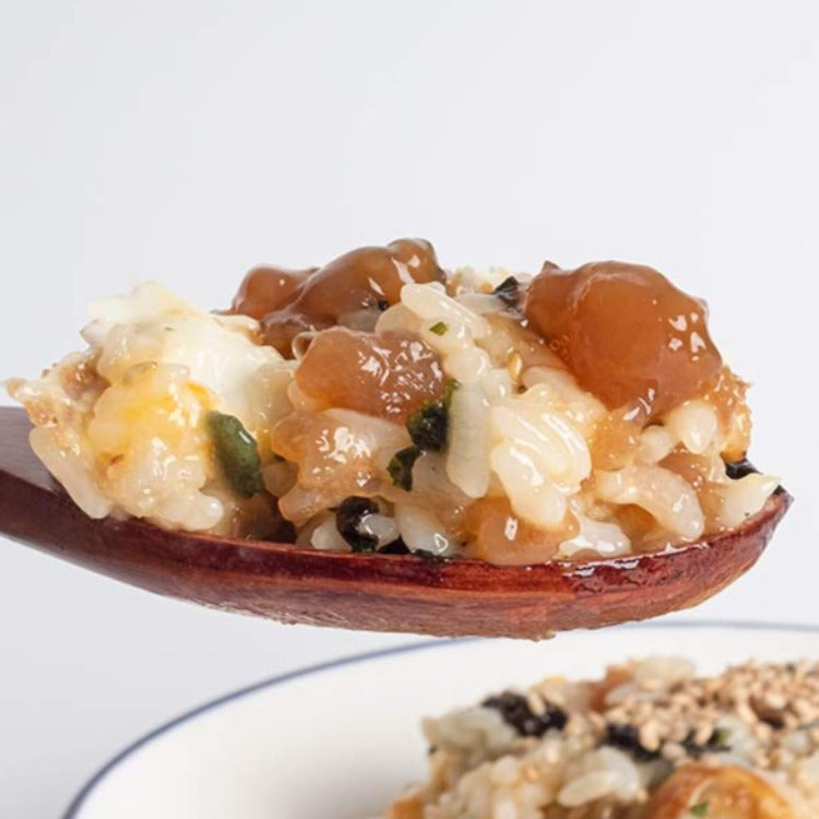 Close-up of a wooden spoon holding a spoonful of rice mixed with Goremi seasoned shrimp with soy sauce. The dish is garnished with sesame seeds and chopped vegetables, emphasizing the rich and savory flavors