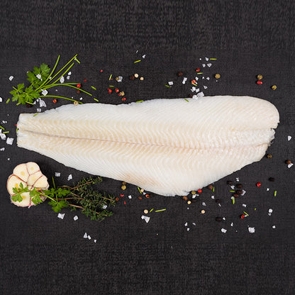 Fresh halibut fillet on a black surface, garnished with herbs and spices, ready for cooking