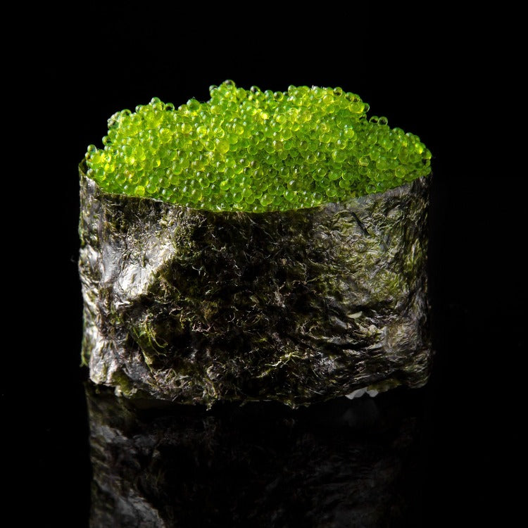 Jalapeno Capelin Roe on a sushi piece wrapped in seaweed, with the vibrant green roe contrasting against the dark seaweed and black background