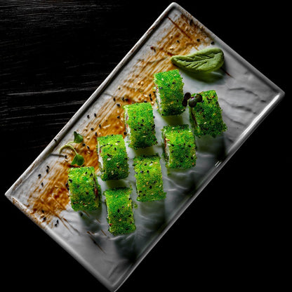 Elegant sushi rolls topped with Jalapeno Capelin Roe, presented on a rectangular white plate with a dark background for a striking contrast