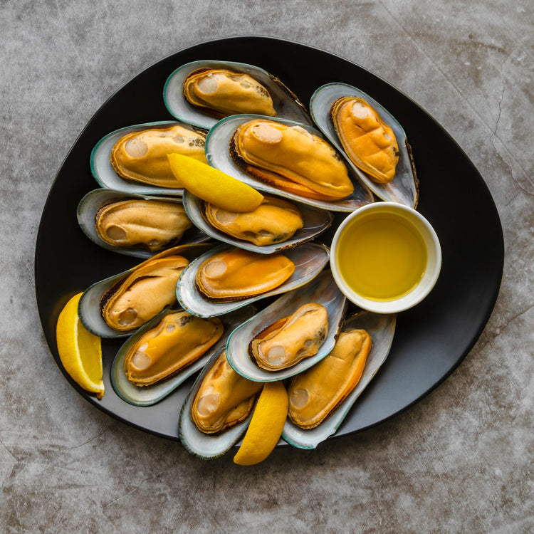 Cooked Mediterranean mussels half shell served with lemon wedges and a side of dipping sauce