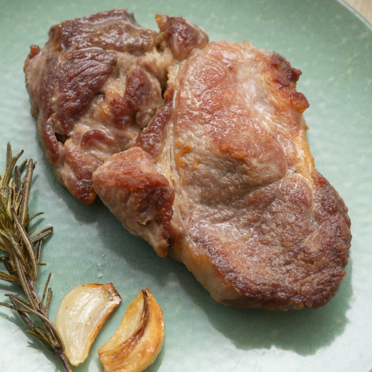 Cooked steak cut pork shoulder on a green plate with garlic and rosemary garnish, highlighting the juicy and tender texture