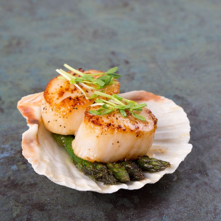 Seared scallops served with asparagus on a half shell, garnished with microgreens