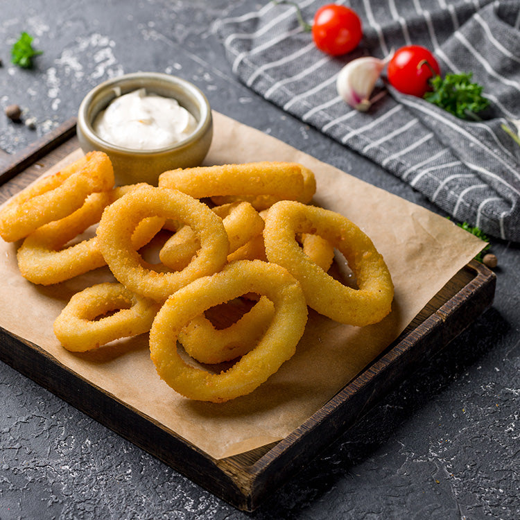 Crispy fried squid rings served on a wooden board with a side of dipping sauce, garnished with garlic and cherry tomatoes