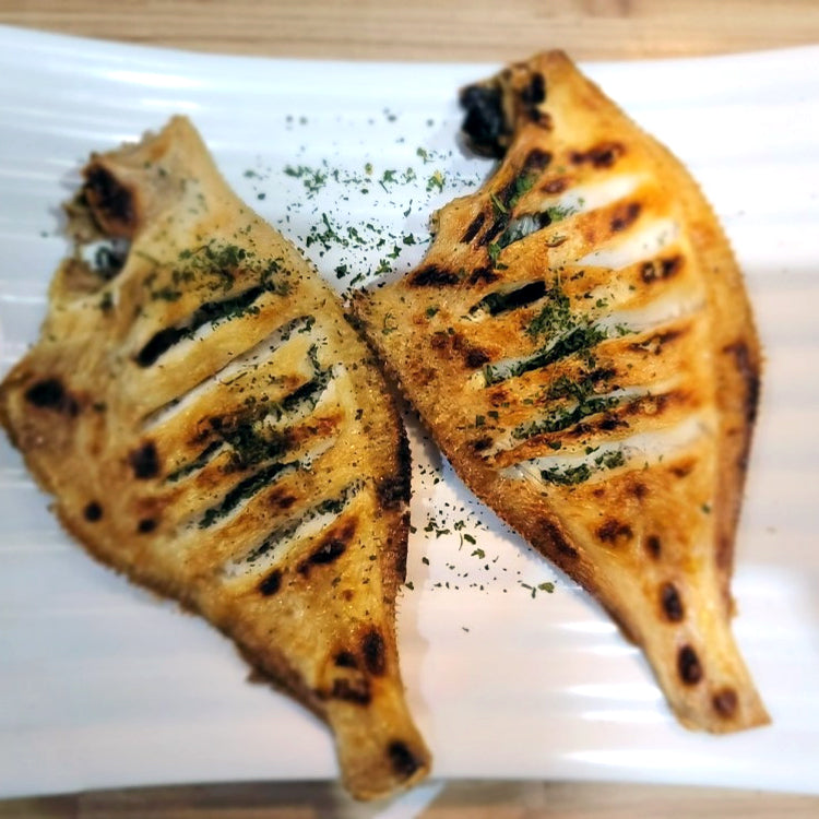 Grilled seasoned yellowfin sole fillets garnished with herbs on a white plate - delicious seafood dish