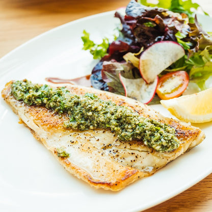 Grilled sea bass fillet served with a side of fresh salad and a lemon wedge