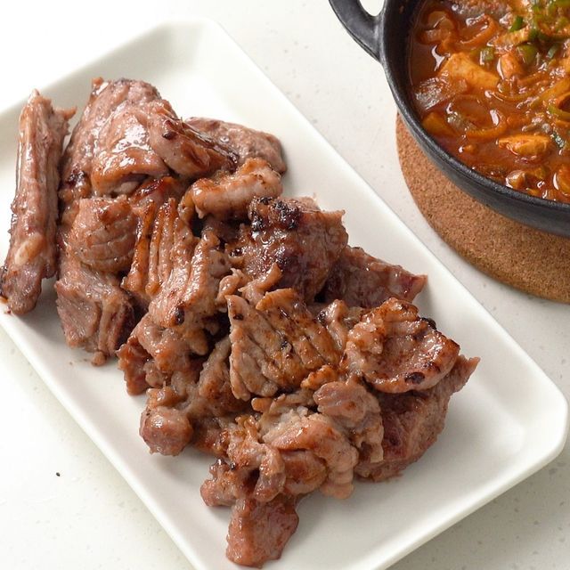 Plate of cooked pork galbi marinated, served alongside a bowl of stew, showcasing the tender and juicy marinated pork pieces