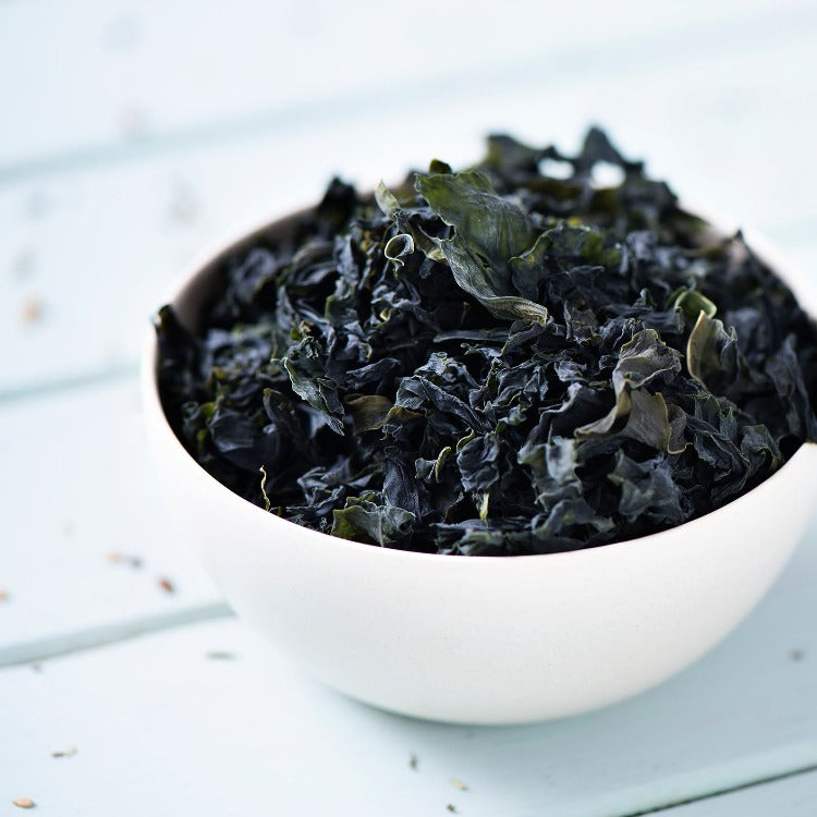 A white bowl filled with dried seaweed, placed on a light blue wooden surface