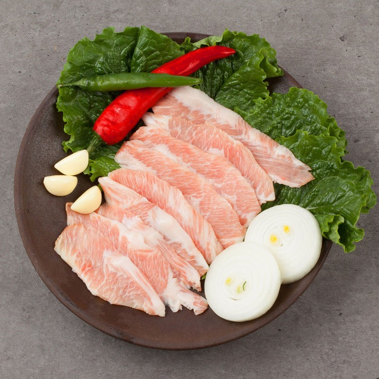 Freshly sliced pork jowl arranged on a rustic brown plate with crisp lettuce, onions, and chili peppers. Perfect for Korean BBQ or flavorful stir-fry dishes