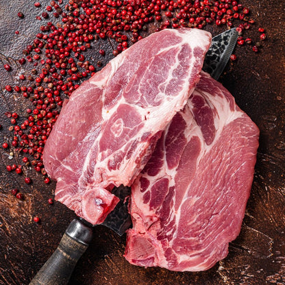 Raw steak cut pork shoulder pieces on a wooden board, surrounded by pink peppercorns, showcasing the fresh marbling and quality of the meat