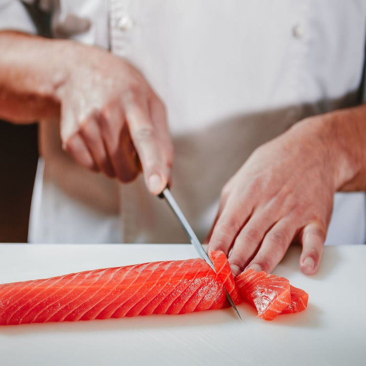 Professional chef meticulously slicing a bright red Sockeye salmon fillet on a white cutting board, demonstrating culinary expertise