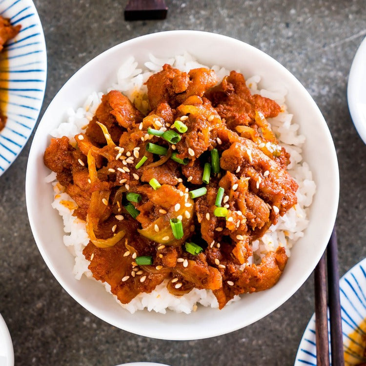 Bowl of spicy pork bulgogi served over steamed rice, topped with green onions and sesame seeds, alongside chopsticks. A delicious and easy-to-prepare meal highlighting Korean cuisine