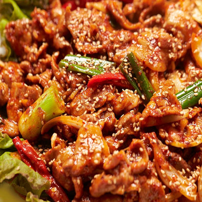 Close-up of cooked spicy pork bulgogi, richly seasoned and garnished with sesame seeds and green onions, served with fresh vegetables. Perfect for a savory Korean-style meal